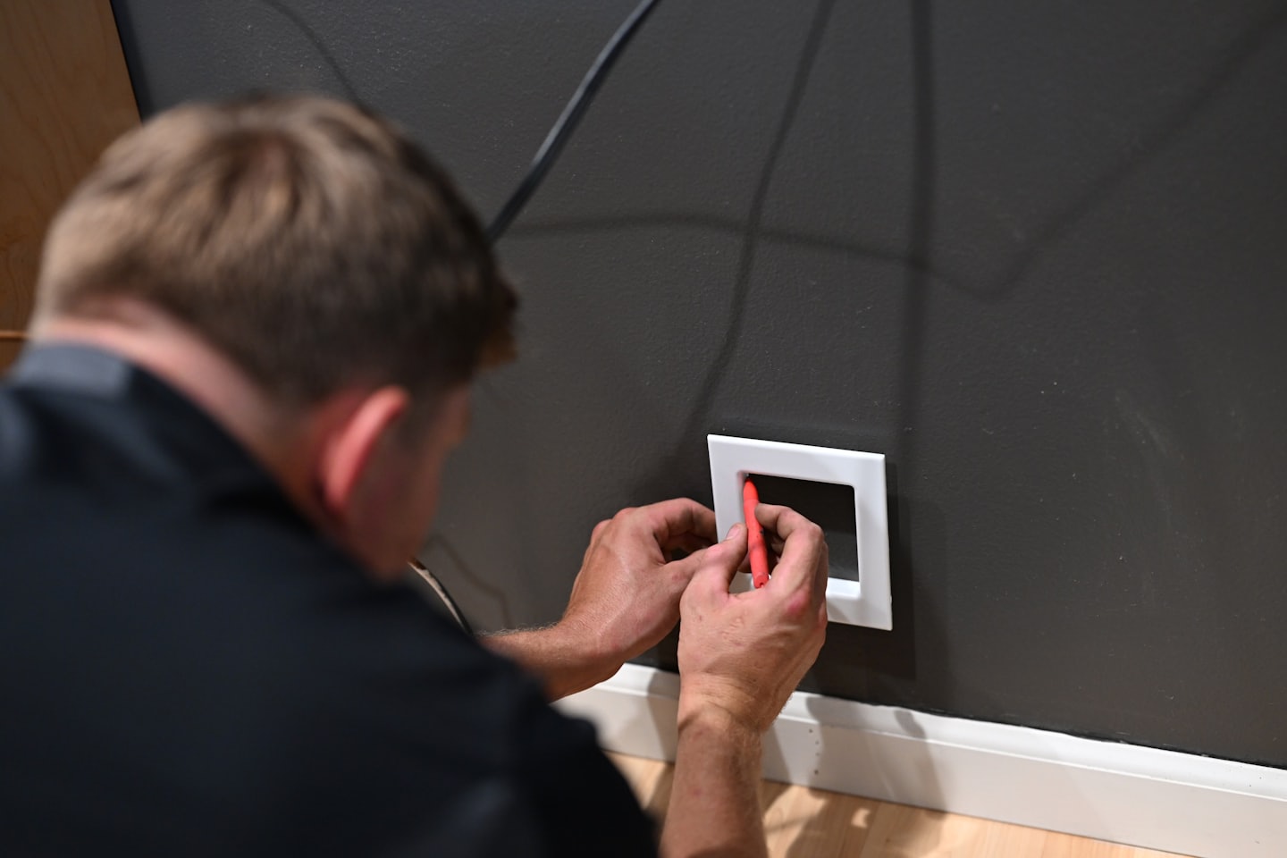Technik montujący puszkę instalacyjną na ścianie za pomocą czerwonego narzędzia.